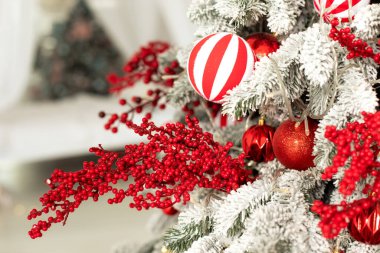 Oyuncak, kırmızı böğürtlen dalları, toplar ve ışık çelenkleriyle süslenmiş Noel ağacı. Oturma odasındaki güzel dekore edilmiş Noel ağacının yakın görüntüsü. Noel süslemeleri konsepti. 
