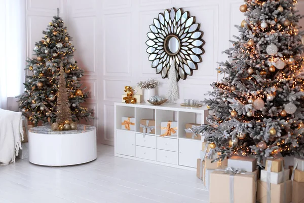 New year winter home decor. A round mirror like sun hangs on wall. Stylish white living room interior with decorated Xmas tree and wooden shelving with festive decor, many gifts. Christmas at home.