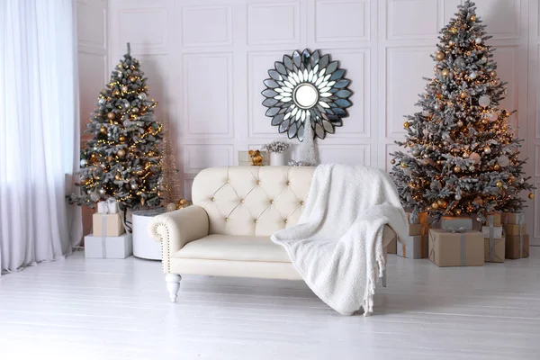 Christmas at home. New year winter home decor. Stylish white living room interior with decorated Xmas tree and sofa with plaid. Stylish round mirror like sun hangs on wall