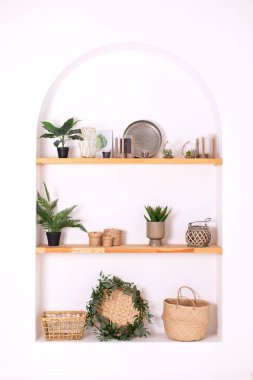 Modern composition of wabi sabi interior with shelf with stylish home decoration. Boho interior of living room and wooden shelves with elegant decor, vase, green houseplants in pots and candles. 