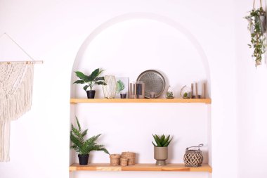 Modern composition of wabi sabi interior with shelf with stylish home decoration. Boho interior of living room and wooden shelves with elegant decor, vase, green houseplants in pots and candles. 