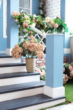 Spring design home with plants and bloom flowers hydrangea in pot on steps. House entrance staircase at home decorated for easter. Wooden porch of house with different flowers. Terrace of summer house