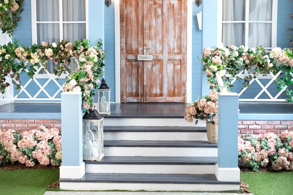 House entrance staircase at home in summer day. Wooden porch of house with different flowers. Terrace of Spring house. Summer design home with bloom flowers and decoration lanterns on steps.