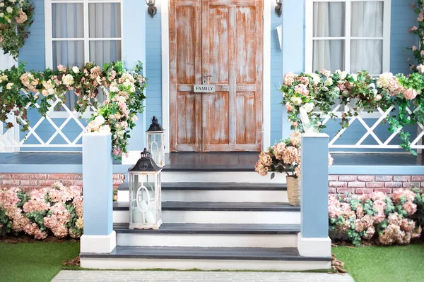 Wooden porch of house with different flowers. Terrace of summer house. Spring design home with bloom flowers and decoration lanterns on steps. House entrance staircase at home decorated for easter.
