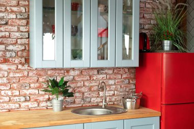 Kitchen with cupboard and drawers and wooden countertop. Facade of wooden blue kitchen in interior at home with modern furniture, red refrigerator, cabinet, cuisine sink and chrome faucet, utensils. 