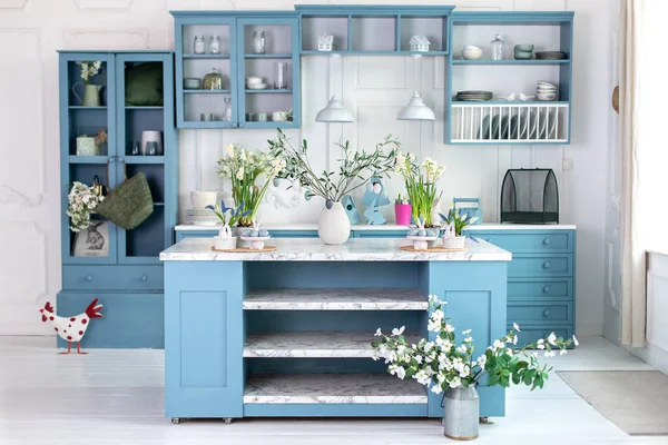 Wooden kitchen in easter decor. Cozy home decor. Kitchen utensils, dishes and plate on table. kitchen island in dining room. Blue kitchen interior with furniture. Stylish cuisine with flowers in vase.