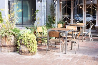 Paris sokaklarının tipik manzarası. Kafe masaları ve saksılarda yeşil bitkiler. Masaları ve sandalyeleri olan boş bir kafe. Lokantanın klasik dış yüzeyi. Caddedeki kahve dükkanı için mobilya.
