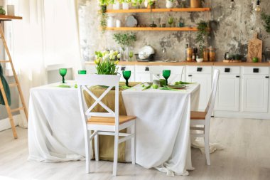 İç tasarım İskandinav mutfağı, masa ve sandalye. Çiçek ve dekorla süslenmiş ahşap kaplama bir mutfak. Mutfak gereçleri, tabaklar raflarda. Mobilyalı şık yemek odası