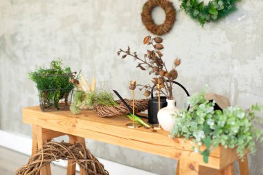 İç işlerinden bir çiçekçi. Üzerinde yeşil bitkiler, kurumuş çiçekler ve gri bir duvarın arka planında bitkiler olan ahşap bir masa. Yazın kırsal tarzda oturma odası. Çiçekçi dükkanı. Düğün dekoru