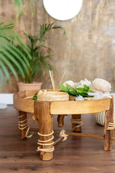 Stylish Rattan coffee table with flowers and accessories in modern home decor. Modern bedroom interior with ethnic decor on design wicker round table. Bedside wooden table. Small cane table