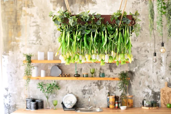 Landscaping of the ceiling in at home. Hanging tulips flowers from the ceiling, wedding decor. Decorative chandeliers decorated with hanging green plants, foliage and greenery. Farmhouse interior
