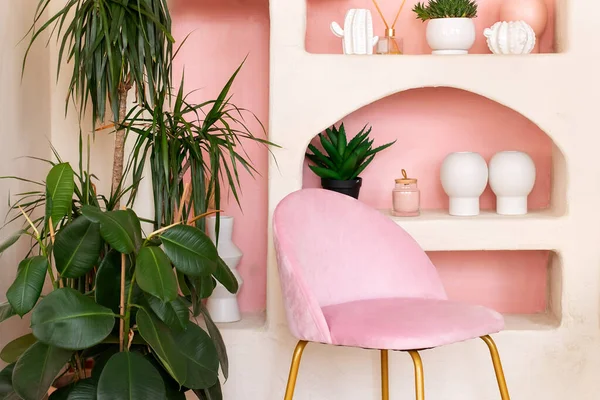 Modern pink composition of wabi sabi interior with arch shelf with home decoration and pink chair. Stylish conceptual interior of living room. Green ficus elastica plants in terracotta pots