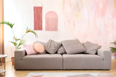 Rahat oturma odası iç tasarımı şık gri kanepe, saksı, halı, yastık ve modern İskandinav ev dekorasyonunda süslemeler. Rahat kanepe ve mobilyalarla modern oda.