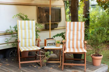 Karavan veya karavan üzerinde kamp alanı yakınında tahta şezlong ve Brown vintage radyo. Bahçede güneşli bir yatak. FM kanalı müzik çalıyor, modaya uygun eski bir radyo çalar ahşap bir masada duruyor.. 