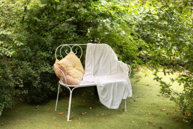 Ekoseli beyaz bank ve yaz bahçesinde dinlenmek için yastık. Klasik dekoratif işlenmiş demir bahçe tezgahı. Samimi bahçe köşesi. Bahçe mobilyalarıyla evin iç avlusu. Sonbahar açık havada dinlenme.