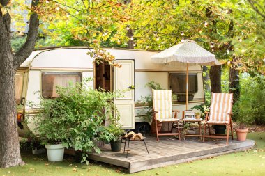 Arka bahçesinde bahçe mobilyaları olan karavan evi. Karavanın dışında iki şezlong var. Karavanda konforlu bir kamp alanı ya da ormanda bir karavan. Karavan karavanı, bahçede kamp yapıyor.. 