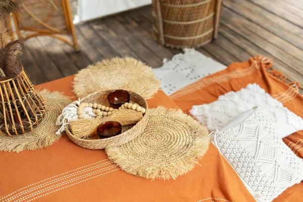 Storage basket, wicker round straw napkins and decorations on orange tablecloth on coffee table. Interior made of natural eco components. Boho style room. Minimalist Scandinavian interior.