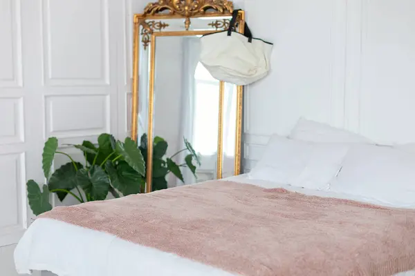 Gold vintage mirror on a white wall background. Interior white bedroom with comfortable bed with plaid and large mirror, copy space. Elegant mirror with beautiful details. scandinavian decoration room