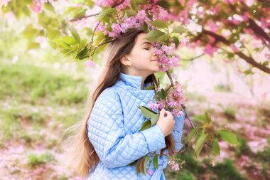 Baharda genç bir kızın portresi, güzel bir yüz, bahçedeki sakura ağacına yakından bak. Gülümseyen kadın kiraz çiçeklerinin tadını çıkarıyor. Çiçek açan ağaç dallı, pembe çiçekli ve doğal güzelliği olan hayalperest kız..