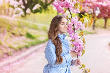 Baharda genç bir kızın portresi, güzel bir yüz, bahçedeki sakura ağacına yakından bak. Gülümseyen kadın kiraz çiçeklerinin tadını çıkarıyor. Çiçek açan ağaç dallı, pembe çiçekli ve doğal güzelliği olan hayalperest kız..