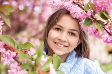 Baharda genç bir kızın portresi, güzel bir yüz, bahçedeki sakura ağacına yakından bak. Gülümseyen kadın kiraz çiçeklerinin tadını çıkarıyor. Çiçek açan ağaç dallı, pembe çiçekli ve doğal güzelliği olan hayalperest kız..