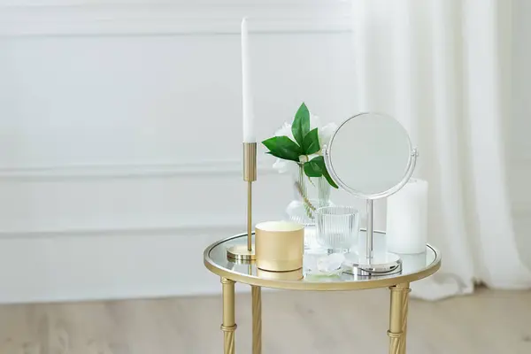 Bathroom accessories. Cosmetic, candles and mirror on table in bathroom. Stylish round mirror on dressing table with cosmetic products, candlestick and vase with flowers. Home interior design decor