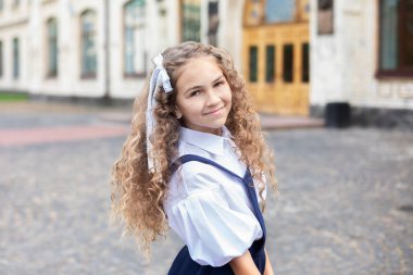 Kıvırcık saçlı güzel bir kız portresi. Arka bahçedeki okulun yanında üniformalı mutlu bir kız. Okula dönelim. Gülümseyen ve kameraya bakan güzel genç kızın yakın yüzü.