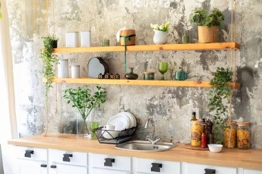 Seramik tabaklar, tencerelerde yeşil bitkiler, tabaklar ve ahşap raflarda rahat bir dekor. Mutfak ahşap rafları ve çeşitli yemek takımları. Mutfakta rafları açın. Skandi beyaz mutfak iç dekorasyonu.. 