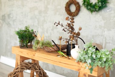 Çiçekçi dükkanı. Düğün dekoru. İç dizayn işyeri çiçekçisi. Üzerinde yeşil bitkiler, çiçekler, sulama tenekesi, bahçe aletleri ve gri bir duvarın arka planında otlar olan ahşap masa.