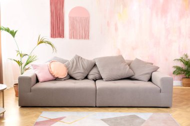 Modern İskandinav evinde şık gri kanepe ve yastıklarla rahat bir oturma odası moda tasarımı. Rahat kanepe ve mobilyalarla modern oda.