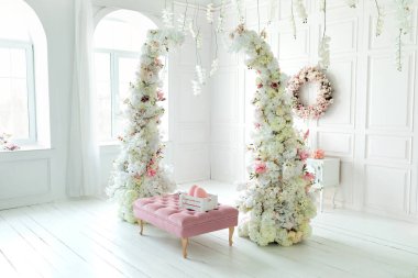 Beyaz oturma odasının içi pembe koltuk puf ve dekoratif çiçek kemeriyle dolu. Tatil bahar dekoru. Duvarında çelenk, çekmece, seramik tavşan ve paskalya yumurtası olan Paskalya bayramı dekorasyonu.