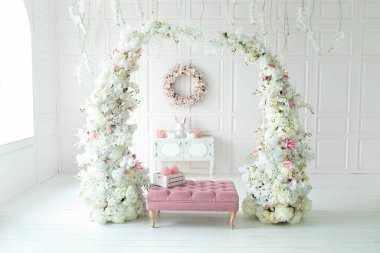 Beyaz oturma odasının içi pembe koltuk puf ve dekoratif çiçek kemeriyle dolu. Tatil bahar dekoru. Duvarında çelenk, çekmece, seramik tavşan ve paskalya yumurtası olan Paskalya bayramı dekorasyonu.