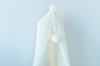 Beyaz tekstil tepe örtüsünü çocukların yatak odasına asmak. Yeni doğan odasının şık bir İskandinav iç tasarımı ve bebek karyolası. Mobilyalı çocuk odası. 