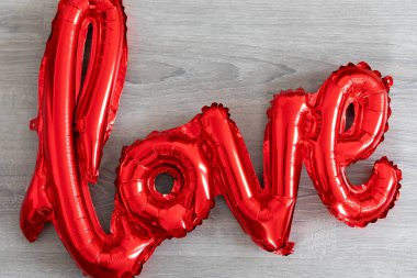 Gri arka planda aşk kelimesi şeklinde kırmızı folyo hava balonu. Aşk konsepti. Tatil, kutlama. Sevgililer Günü ya da düğün, bekarlığa veda partisi, doğum günü süsü. İç tasarım odası.