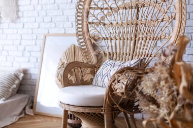 Rattan tavus kuşu hasır koltuğu yastıklı, büyük çerçeve posteri, kurutulmuş çiçekler ve beyaz tuğla duvarın yanındaki oturma odasında bitkiler. Wabi Sabi odasının iç tasarımı. Eko doğal mobilya. 