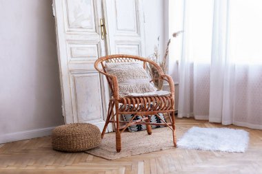 İç tasarımı olan modern boho odası, rattan koltuğu ve beyaz duvarın yanındaki dekoratif klasik kapısı. Oturma odasında yastıklı hasır tahta sandalye. Eko mobilyalar, geniş bir yatak odasında doğal mobilyalar.