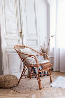 İç tasarımı olan modern boho odası, rattan koltuğu ve beyaz duvarın yanındaki dekoratif klasik kapısı. Oturma odasında yastıklı hasır tahta sandalye. Eko mobilyalar, geniş bir yatak odasında doğal mobilyalar.