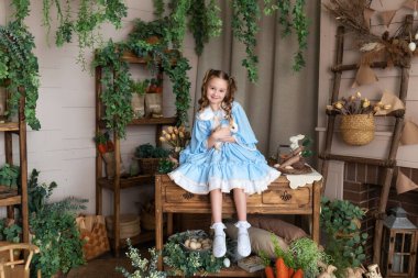 Mavi elbiseli genç kız Paskalya tavşanı ile oynuyor. Bir çocuk gerçek bir tavşanı kollarında tutarken Paskalya 'nın iç odasının arka planına yaslanır. Çocuk ve hayvan. Küçük Çiftçi. Hayvan konsepti