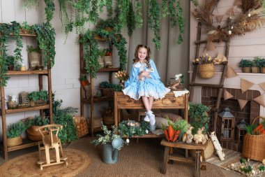 Mavi elbiseli genç kız Paskalya tavşanı ile oynuyor. Bir çocuk gerçek bir tavşanı kollarında tutarken Paskalya 'nın iç odasının arka planına yaslanır. Çocuk ve hayvan. Küçük Çiftçi. Hayvan konsepti