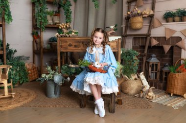 Mavi elbiseli genç kız Paskalya tavşanı ile oynuyor. Bir çocuk gerçek bir tavşanı kollarında tutarken Paskalya 'nın iç odasının arka planına yaslanır. Sevimli Çocuk ve Hayvan. Hayvan sevgisi konsepti