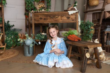 Mavi elbiseli genç kız Paskalya tavşanı ile oynuyor. Bir çocuk gerçek bir tavşanı kollarında tutarken Paskalya 'nın iç odasının arka planına yaslanır. Sevimli Çocuk ve Hayvan. Hayvan sevgisi konsepti