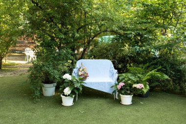 Bahçeli evin iç avlusu. Hortensiya çiçekleriyle süslenmiş, saksılarda bitkiler. Yaz bahçesinde ekose ve sepetli beyaz işlemeli demir bir bank. Rahatlamak için. Samimi dış bahçe köşesi.