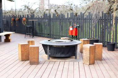 Bahçedeki demir ateş çukuru. Bahçede oturmak için büyük kütükleri olan metal siyah şömine kasesi. Açık hava partisi için şömine etrafında siyah ateş çelik çukur. İçinde alevler olan ızgara. tablo pişirme yüzeyi. 