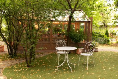 Bahçede sonbahar atmosferi - masa, sandalyeler ve düşmüş sarı yapraklar. Bahçe mobilyalarının olduğu arka bahçe. Evdeki rahat teras. Beyaz demir sandalyeler ve dışarıda ya da dışarıda dinlenmek için masa.. 