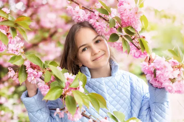 Baharda genç bir kızın portresi, güzel bir yüz, bahçedeki sakura ağacına yakından bak. Gülümseyen kadın kiraz çiçeklerinin tadını çıkarıyor. Çiçek açan ağaç dallı, pembe çiçekli ve doğal güzelliği olan hayalperest kız..