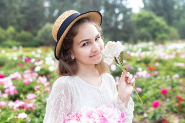 Yakından bakınca, beyaz elbiseli güzel bir kız ve şakayık tarlasında çiçeklerle yürüyen hasır bir şapka. Gülümseyen mutlu kız çiçek tutan pembe şakayık çiçekli bahçede