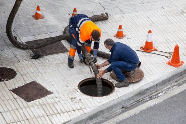 Galiçya, İspanya; 30 Eylül 2022: İki işçi bir hortumla kanalizasyonun önünü açıyor