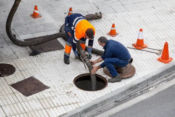 stock image Galicia, Spain; september 30, 2022: Two workers on city street unblocking a sewer with a hosepipe