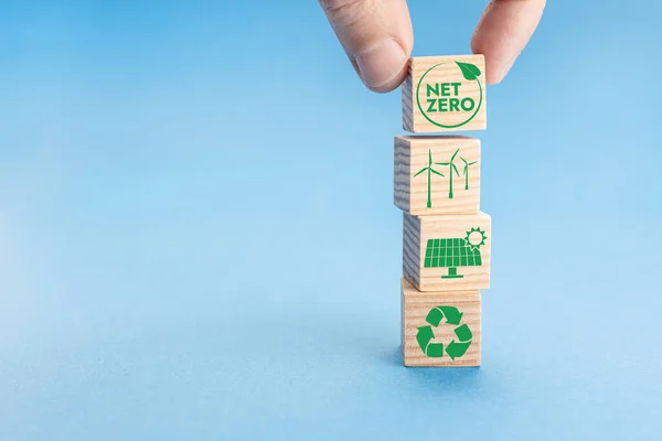 Net Zero and Carbon Neutral Concept. Hand putting wood block with Net Zero icon on top of others with green energy icons. Blue background. Copy space
