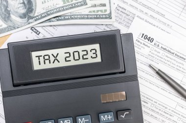 Tax time 2023 concept. Text on calculator screen, tex forms and dollar banknotes on table. Top view